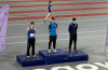 Photograph from above of three teenage boys in sports kit standing on the 1, 2, 3 winners' podium at an athletics track