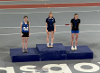 Photograph from above of three teenage girls in sports kit standing on the 1, 2, 3 winners' podium at an athletics track