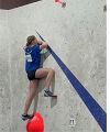 A teenager on a climbing wall during competition. She is roped in and wearing a harness.